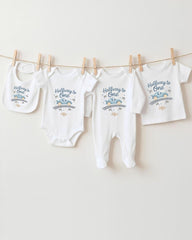 A row of four white baby clothes, including onesies and pajamas, hanging on a clothesline.