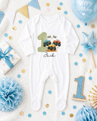 A white onesie with a truck design, surrounded by birthday decorations and a blue balloon with the text "Happy Birthday".