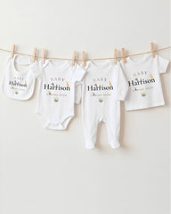 A row of four white baby clothes with the name "Baby Harrison" printed on them, hanging on a clothesline.