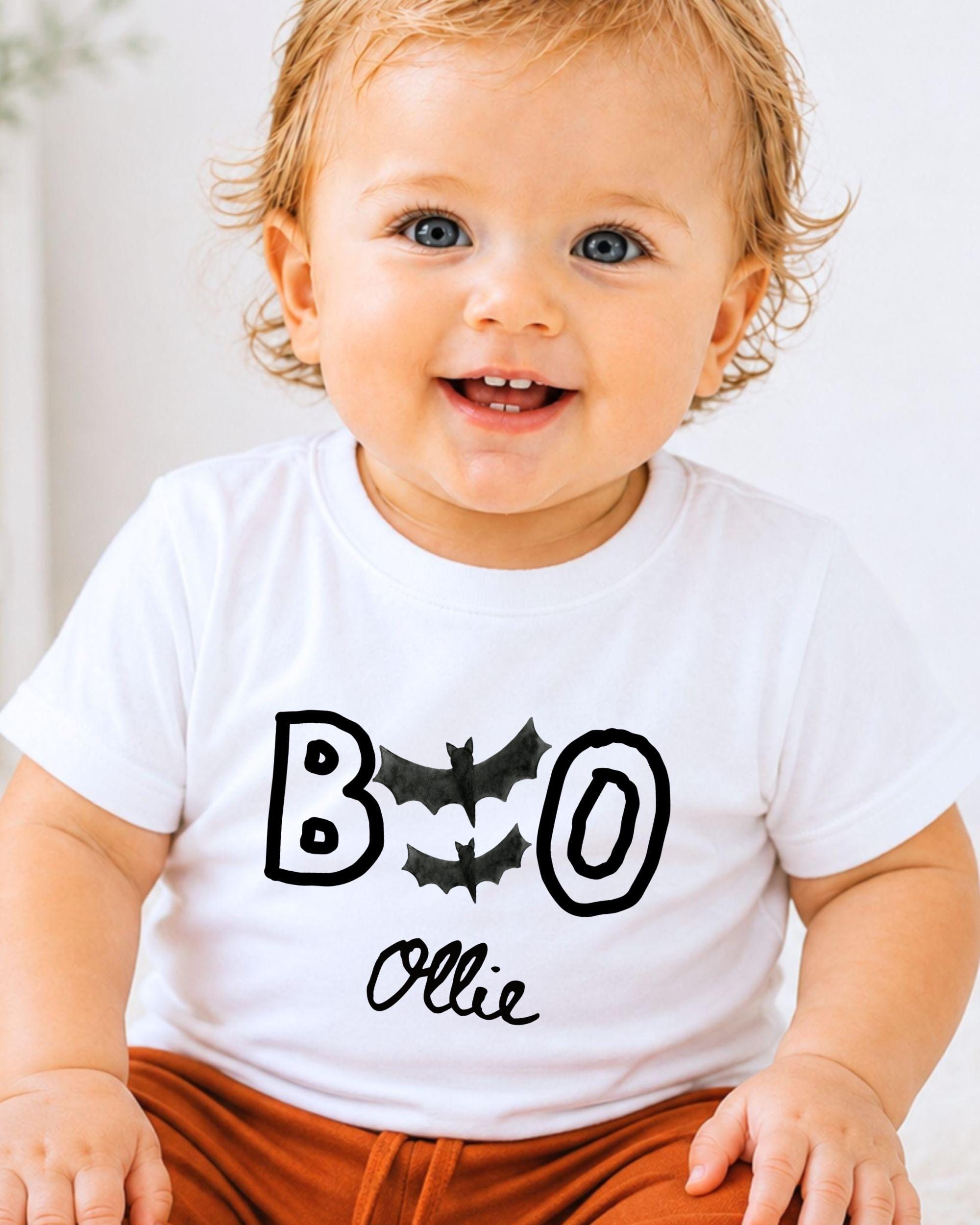 A smiling baby boy wearing a white t-shirt with the text "BOO OLLIE" printed on it.