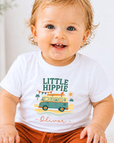 A smiling baby boy wearing a white t-shirt with a colorful graphic design and text.