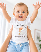 A smiling baby wearing a white t-shirt with a personalized message and an elephant graphic, being held up by someone's arms.
