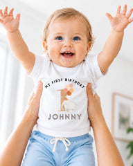 A smiling baby wearing a white t-shirt with a personalized message and an elephant graphic, being held up by someone's arms.