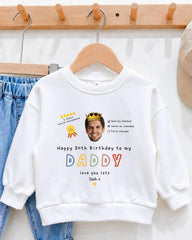 A white sweatshirt with a personalized message and a crown image on it, hanging on a wooden hanger.