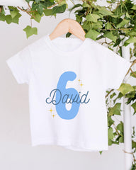 A white t-shirt with the number 6 and the name "David" printed on it, hanging on a wooden hanger.