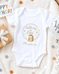 A white onesie with a hedgehog design and the text "Halfway to One Mario" printed on it, along with a "Happy Birthday" sign and confetti.