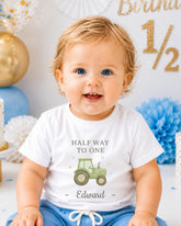 A smiling baby boy wearing a white t-shirt with a tractor graphic and the text "Half Way to One Edward" printed on it.