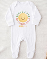 A white onesie with a smiley face design and text printed on it.