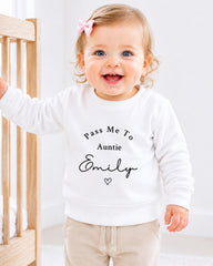 A smiling baby girl wearing a white sweater with the text "Pass Me To Auntie Emily" printed on it.