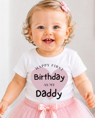 A smiling baby girl wearing a white t-shirt with text and a pink heart, standing in front of a white background.