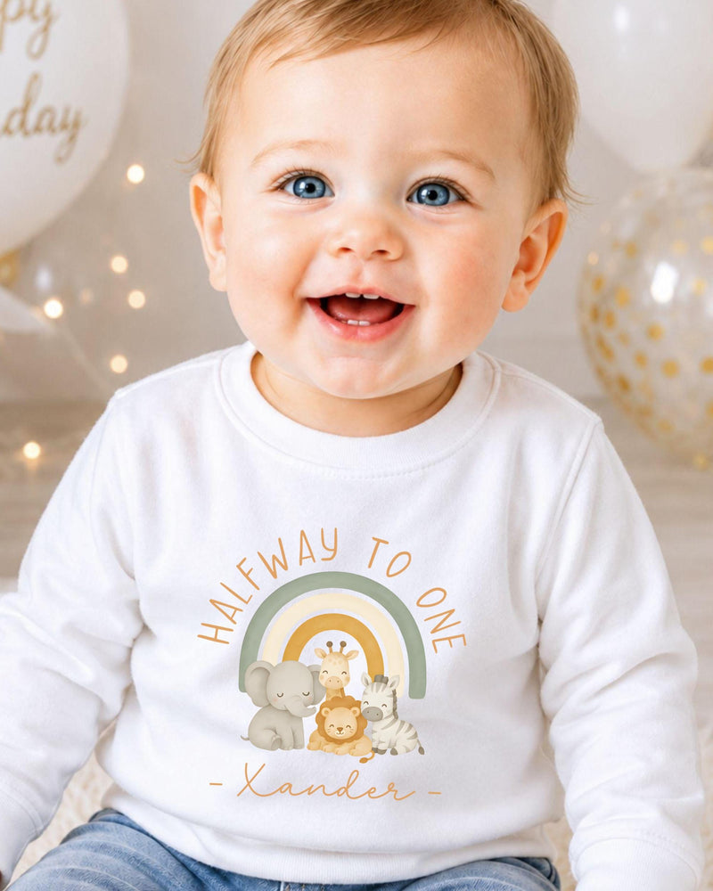 A smiling baby wearing a white shirt with a graphic of animals and the text "Halfway to one" printed on it.