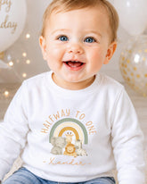 A smiling baby wearing a white shirt with a graphic of animals and the text "Halfway to one" printed on it.