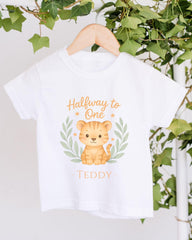 A white t-shirt with a cartoon tiger graphic and the text "Halfway to One" printed on it, hanging on a wooden hanger.