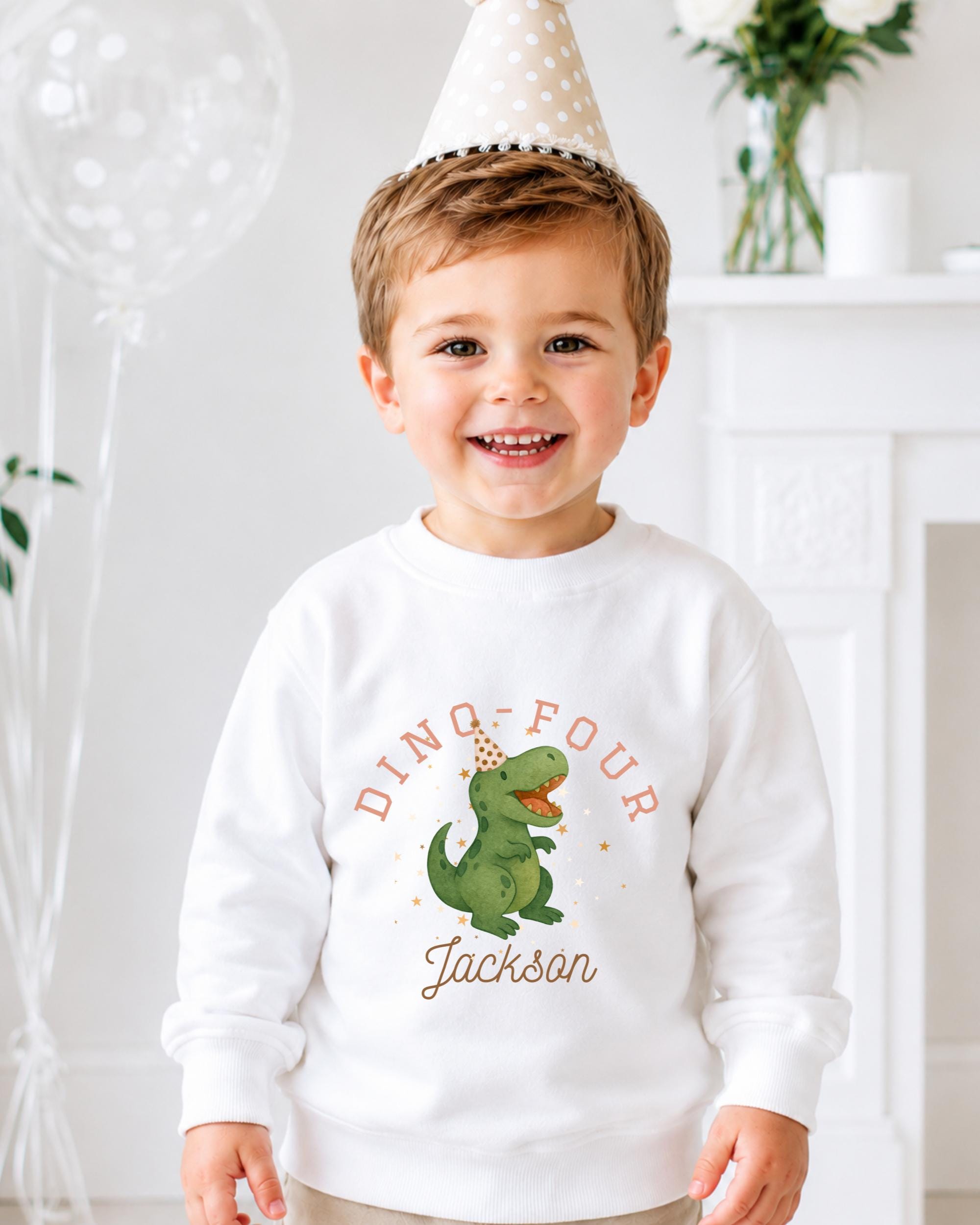 A young boy wearing a white sweatshirt with a dinosaur graphic and the text "DINO-FOUR JACKSON" is smiling at the camera.