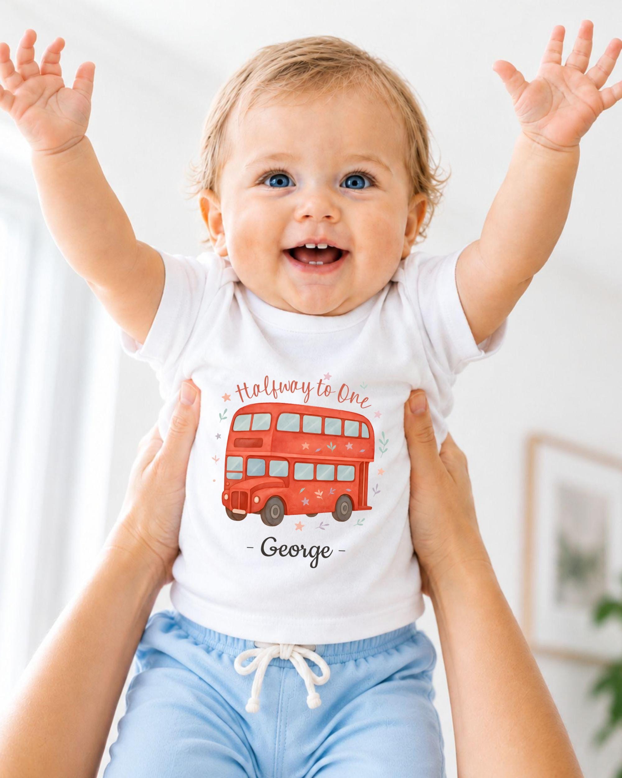 A smiling baby wearing a white t-shirt with a red double-decker bus design and blue shorts, with their arms raised in a joyful gesture.
