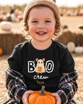 A young child wearing a black t-shirt with a ghost character and the text "BOO crew Tom" is holding a small pumpkin.