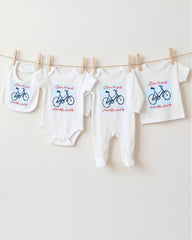 A row of baby clothes, including onesies and bibs, hanging on a clothesline.