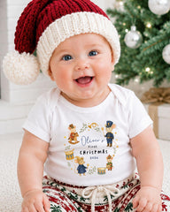A smiling baby wearing a Santa hat and a t-shirt with a Christmas-themed design.