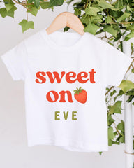A white t-shirt with the text "Sweet on Eve" printed on it, along with a strawberry graphic.
