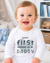 A smiling baby wearing a white onesie with text that says "Happy first birthday as my Daddy".