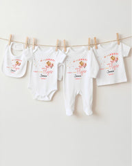 A row of four white baby clothes, including onesies and bibs, hanging on a clothesline.