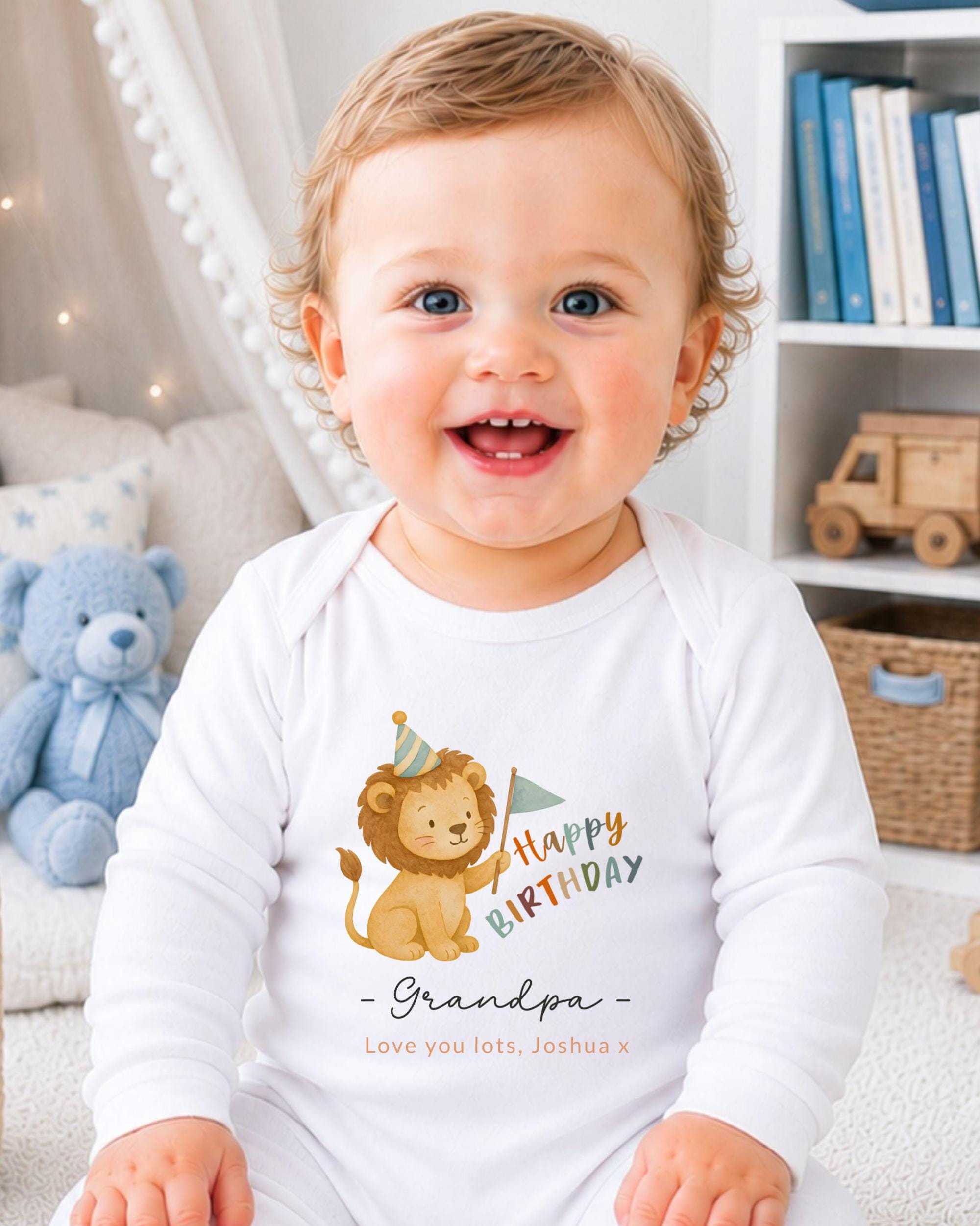 A smiling baby wearing a white onesie with a cartoon lion and the text "Happy Birthday Grandpa" printed on it.