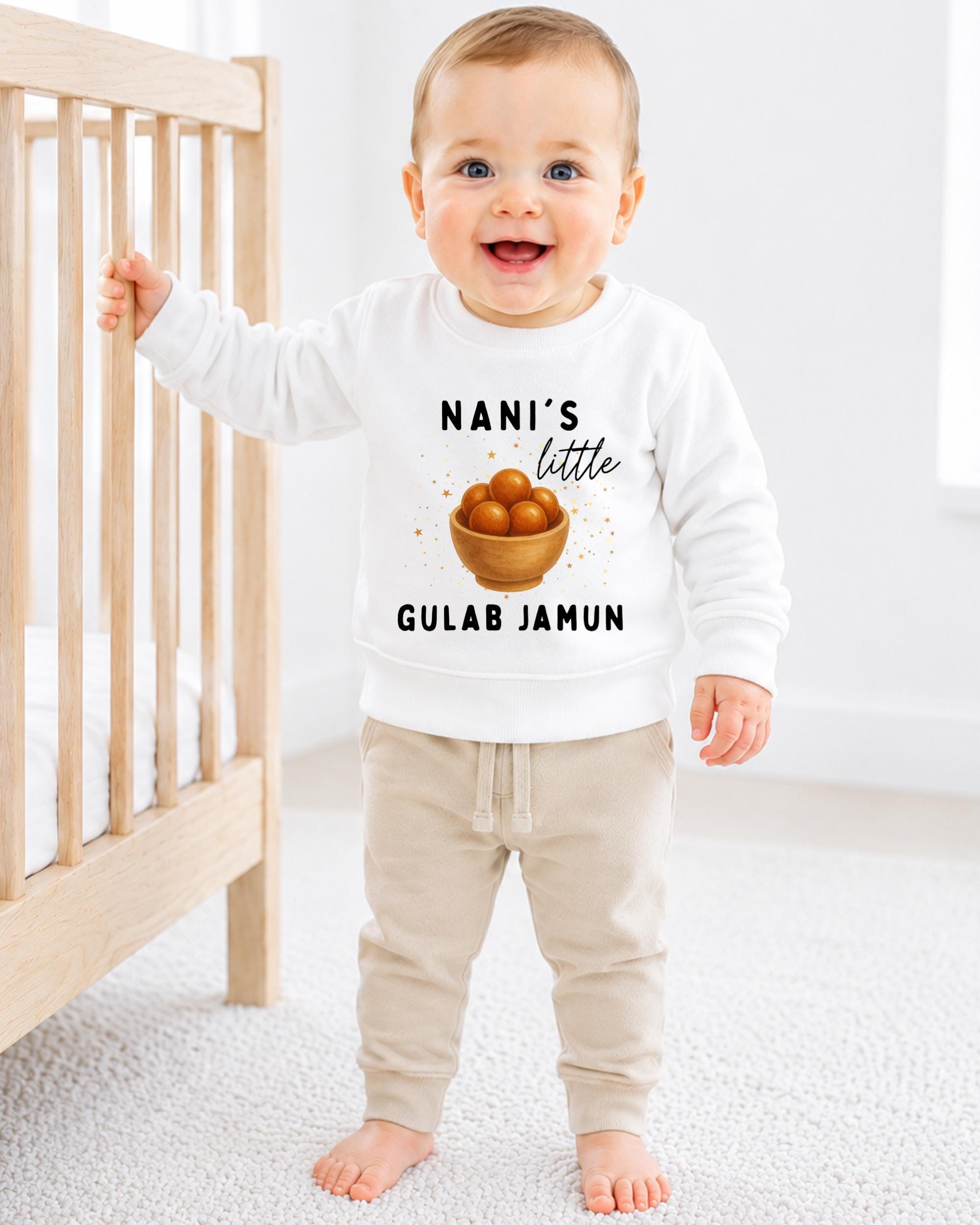 A smiling baby boy wearing a white sweatshirt with a graphic of a bowl of fruit and the text "NANI'S LITTLE GULAB JAMUN" printed on it.
