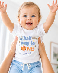 A smiling baby wearing a white t-shirt with a birthday message and a tiger graphic, being held up by someone's arms.