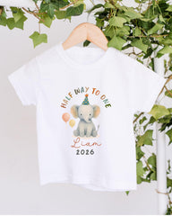 A white t-shirt with a graphic design featuring a cartoon elephant wearing a party hat and balloons, along with the text "Half way to one" and "Liam 2026".