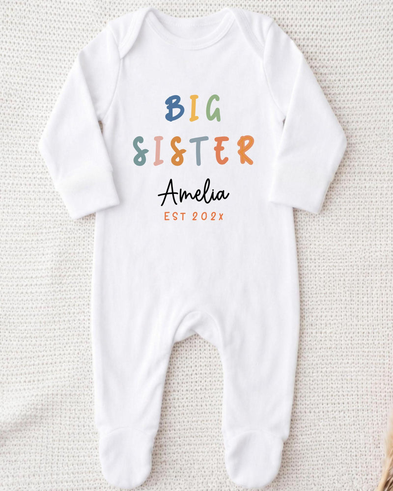 A white bodysuit with the text "BIG SISTER Amelia EST 202x" printed on it.