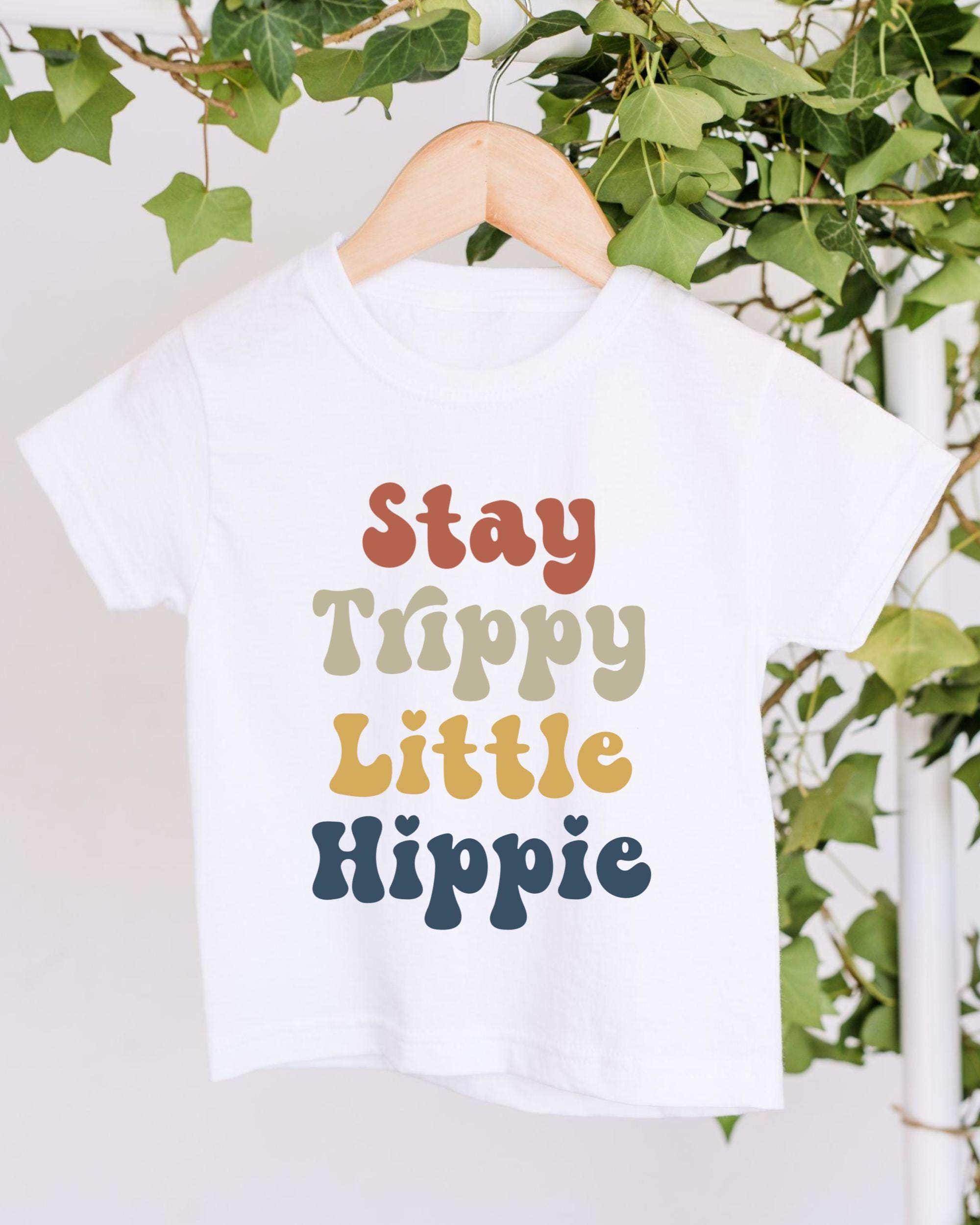 A white t-shirt with colorful text printed on it, hanging on a wooden hanger.