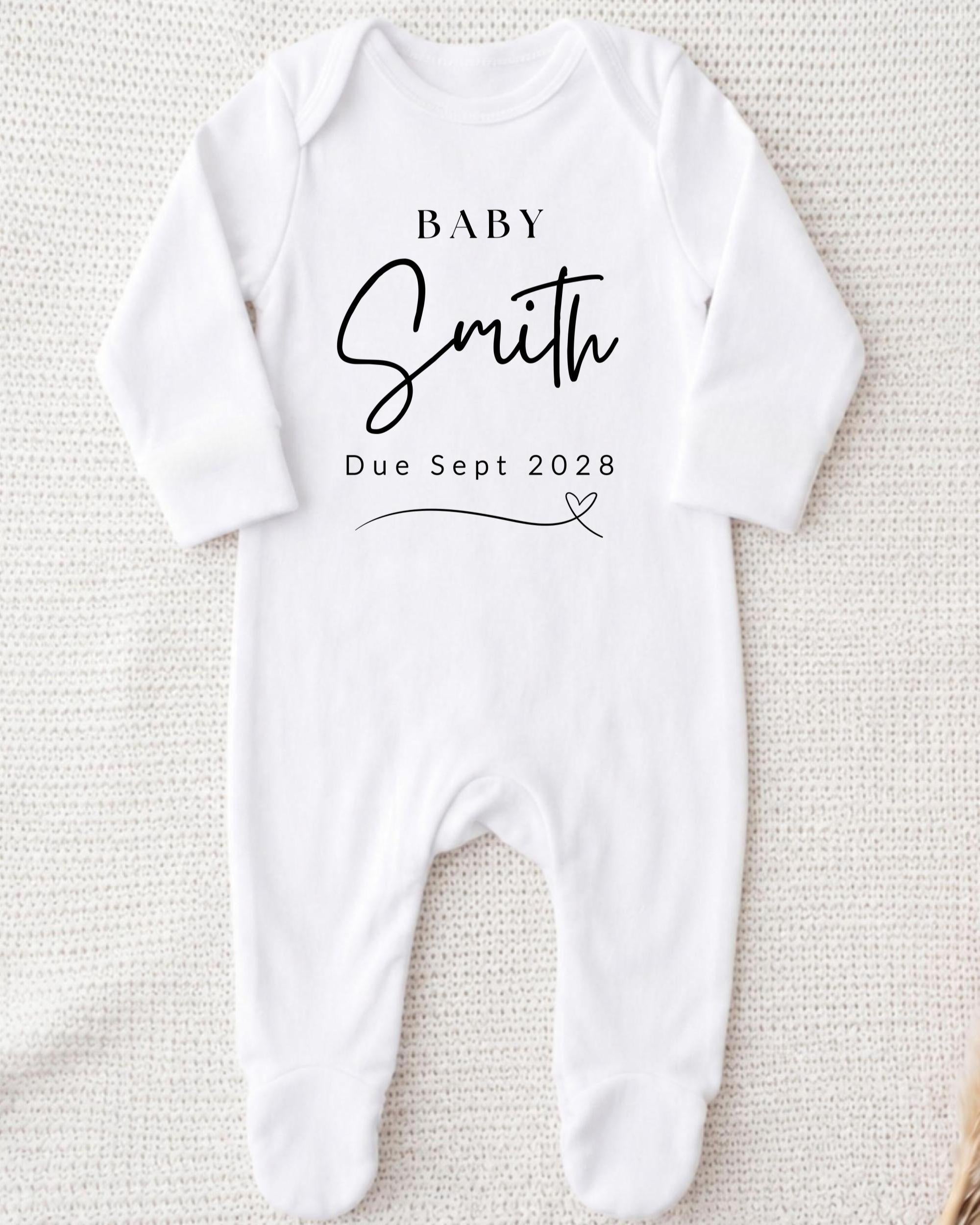 A white onesie with the text "BABY Smith Due Sept 2028" printed on it.