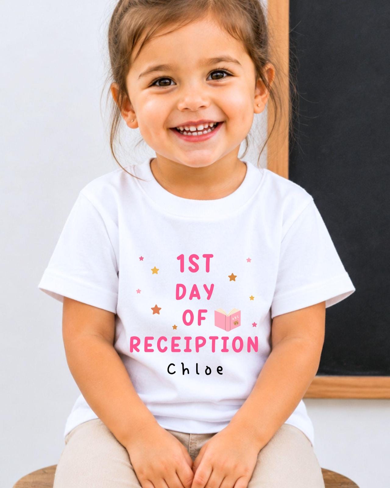 A young girl wearing a white t-shirt with text and a small illustration, smiling at the camera.