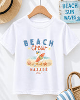 A white t-shirt with a beach-themed graphic design, including a surfer, beach elements, and text that says "BEACH CREW".