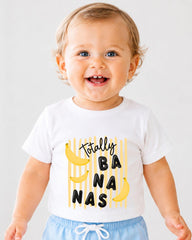 A smiling baby wearing a white t-shirt with a playful graphic design featuring bananas and the text "Totally Banana".