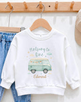 A white sweatshirt with a graphic design of a van and the text "Halfway to One" printed on it, hanging on a wooden hanger.