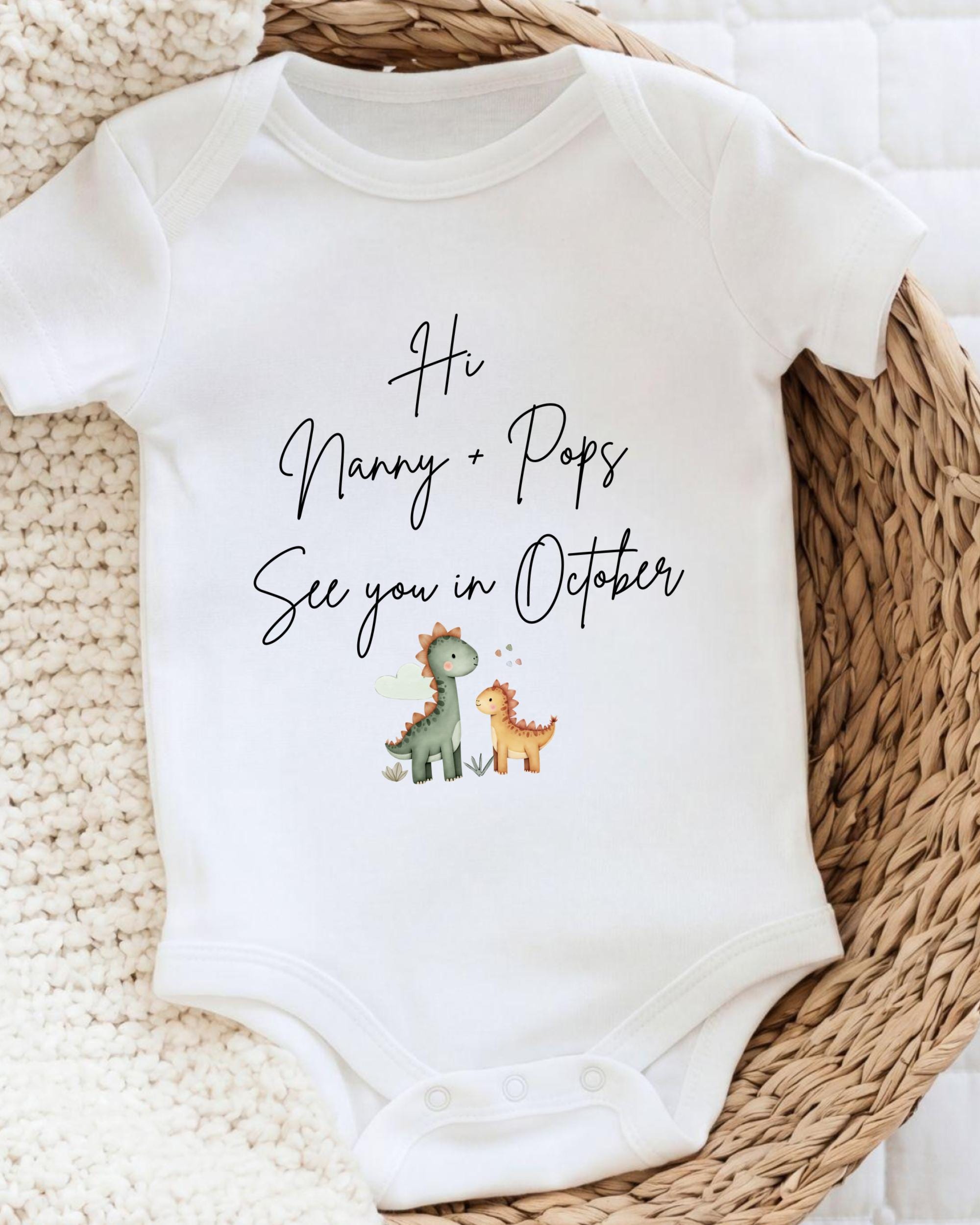A white baby onesie with a personalized message printed on it, placed on a woven basket.