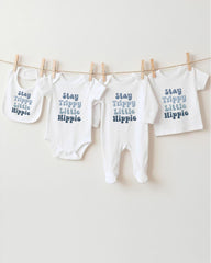 A row of four white baby clothes with the text "Stay Trippy Little Hippie" printed on them, hanging on a clothesline.