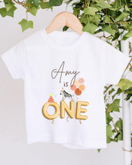 A white t-shirt with a birthday-themed design hanging on a wooden hanger.