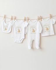 A row of four white baby clothes, including onesies and bibs, hanging on a clothesline.