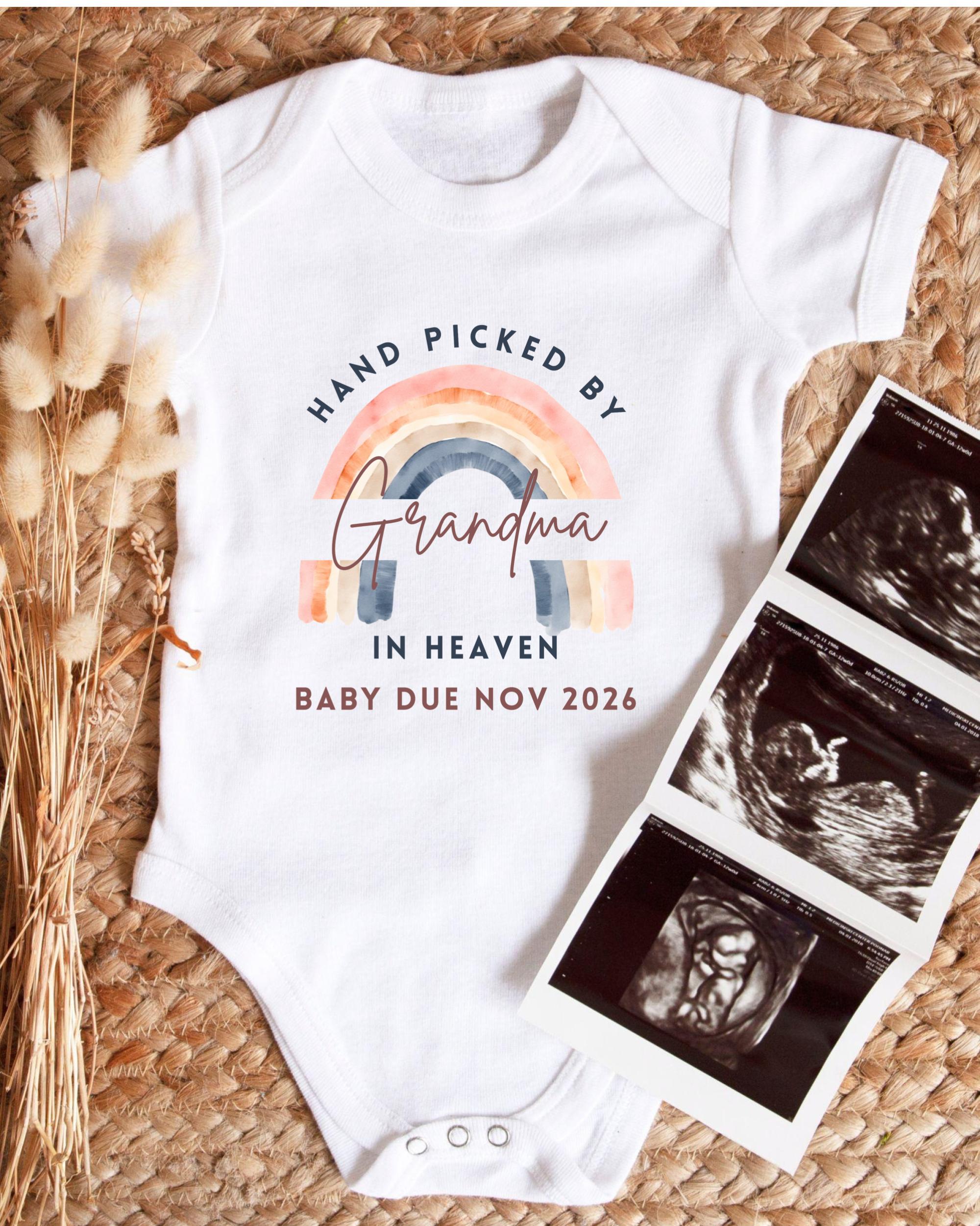 A white baby onesie with a rainbow graphic and text that says "HAND PICKED BY Grandma in Heaven BABY DUE NOV 2026" is displayed alongside a set of three black and white baby ultrasound images.