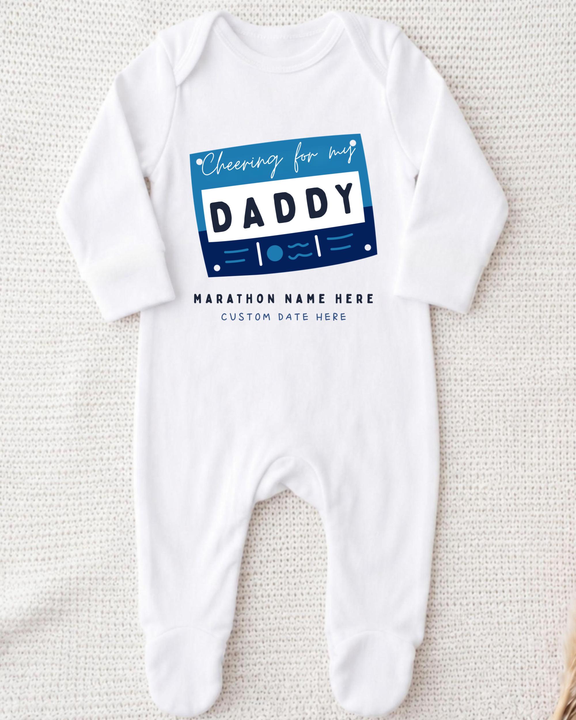 A white onesie with a graphic design on it, featuring the text "Cheering for my DADDY" and "MARCHON NAME HERE" along with a custom date field.