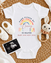 A baby onesie with a rainbow design and text, a pair of white crocheted bunny slippers, and an Ultrasound image of a baby.
