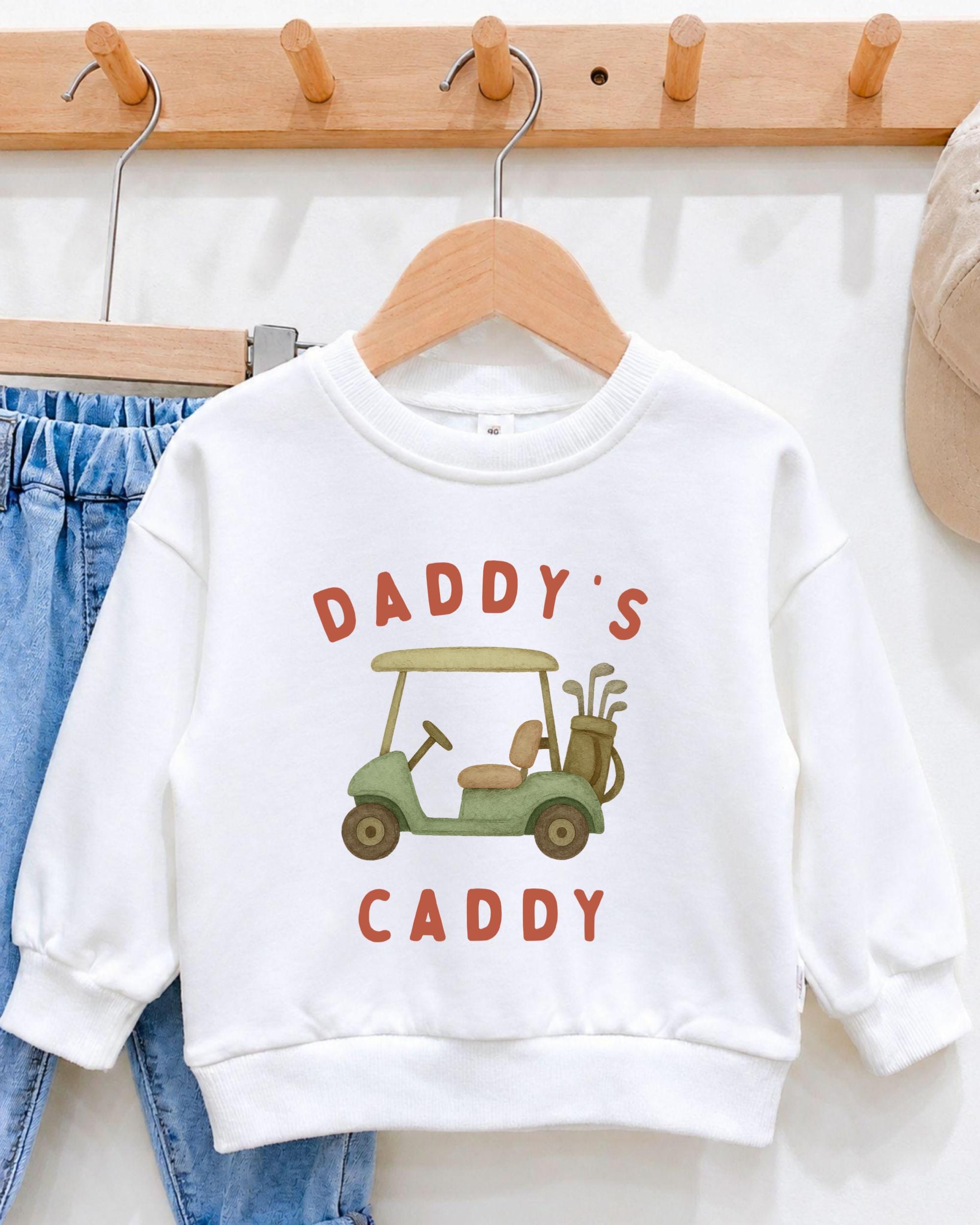 A white sweatshirt with a graphic of a golf cart and the text "DADRY'S CADDY" printed on it.