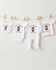 A collection of white baby clothes, including onesies and bibs, with a cartoon character printed on them. The clothes are hanging on a clothesline, and there are four of them in total.
