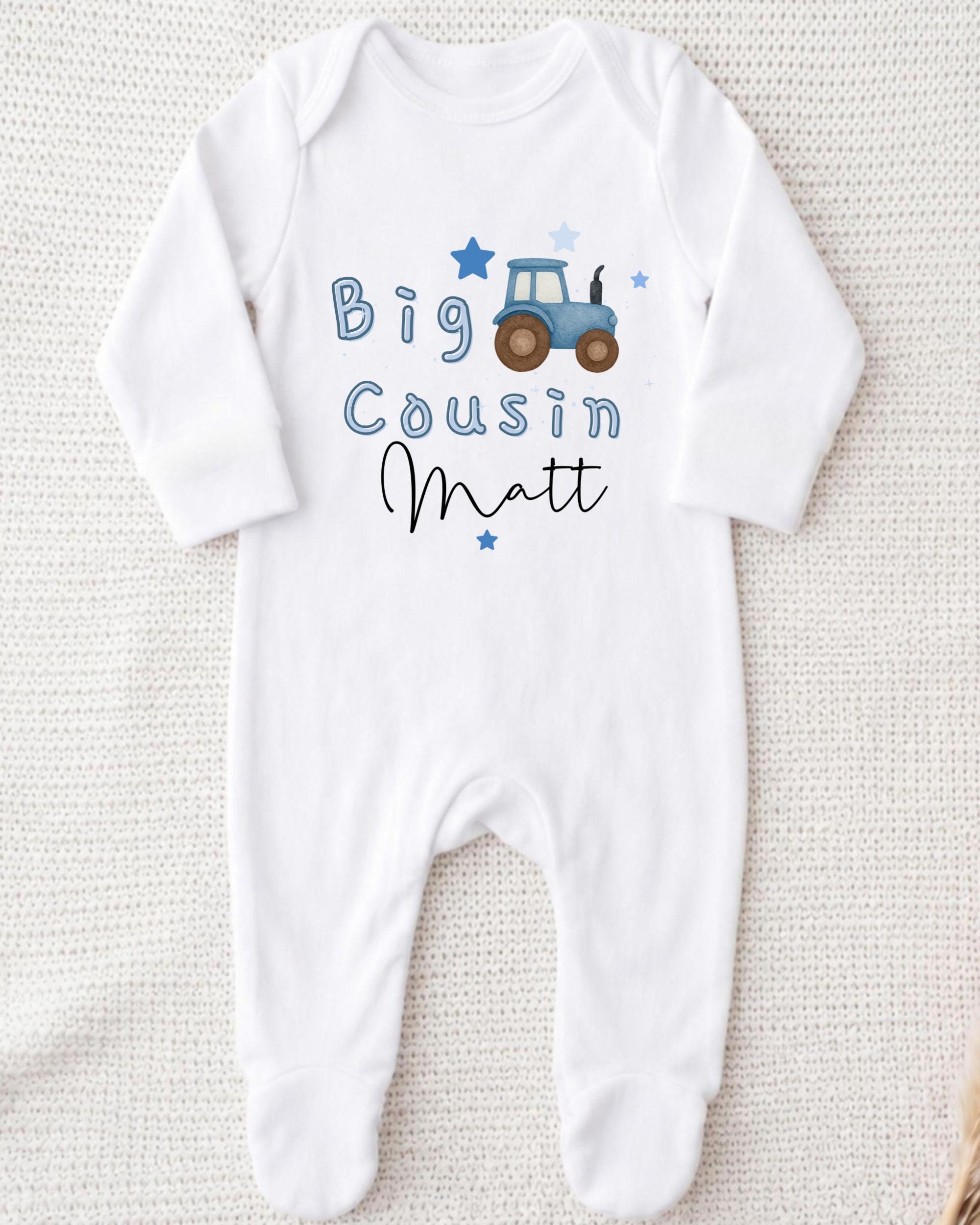 A white onesie with a tractor graphic and the text "Big Cousin Matt" printed on it.