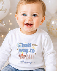 A smiling baby boy wearing a white shirt with a birthday message and a cartoon character.