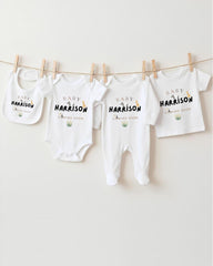 A row of four white baby clothes with the name "Baby Harrison" printed on them, hanging on a clothesline.