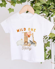 A white t-shirt with a graphic design featuring a giraffe, elephant, and other animals, along with the text "Wild One Henry".