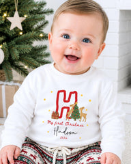 A smiling baby boy wearing a white sweatshirt with a personalized Christmas-themed design.
